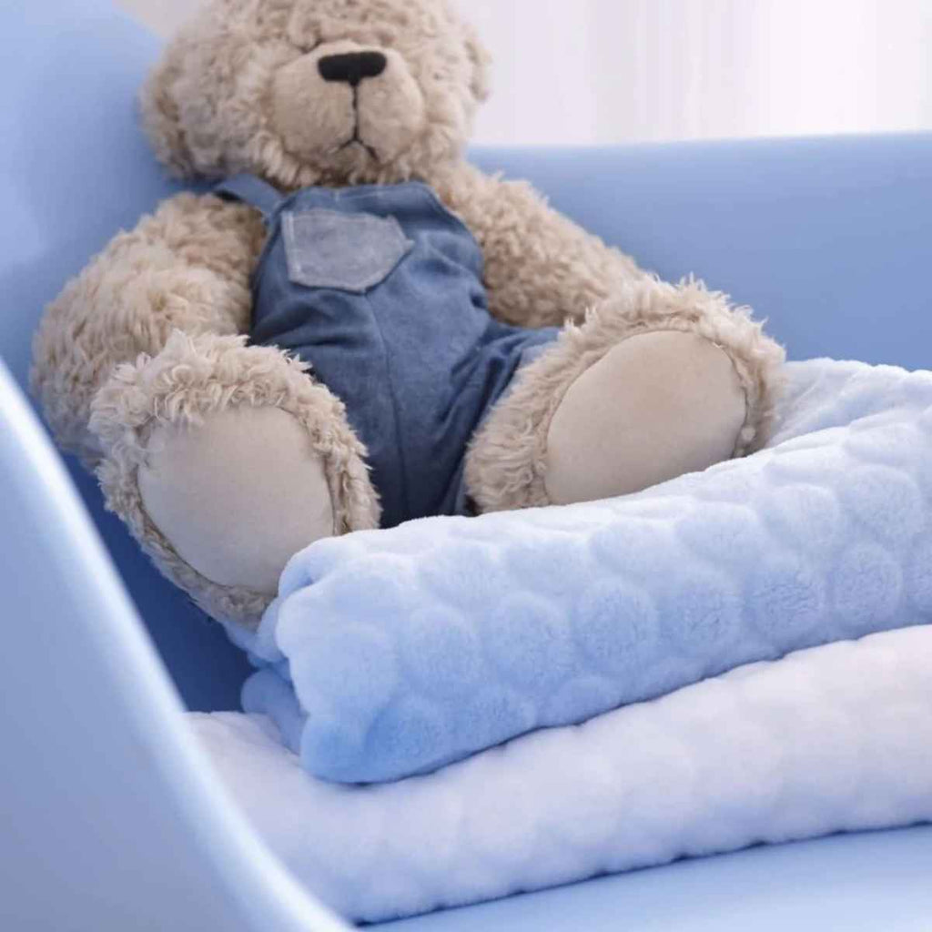 Teddy bear wearing denim overalls sitting on a blue marshmallow blanket