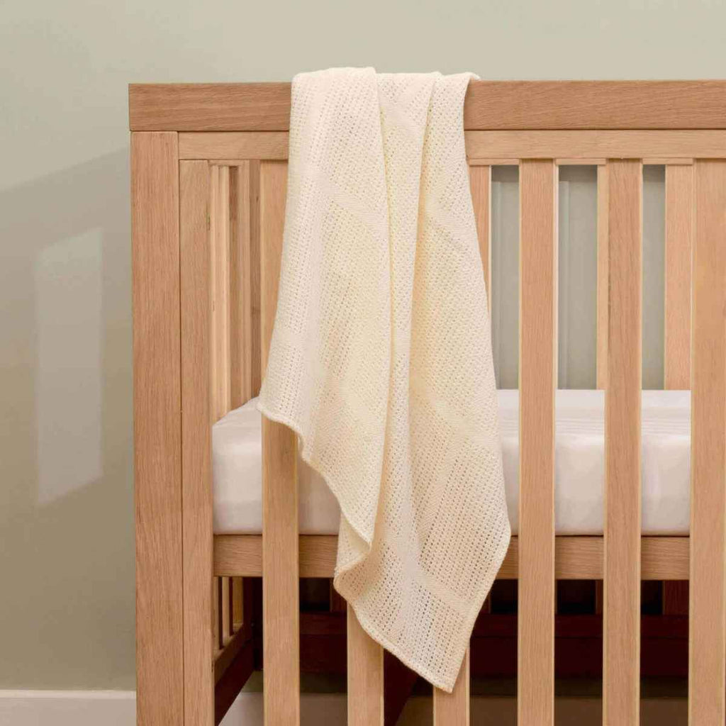 Wooden cot with a cream baby blanket draped over the side
