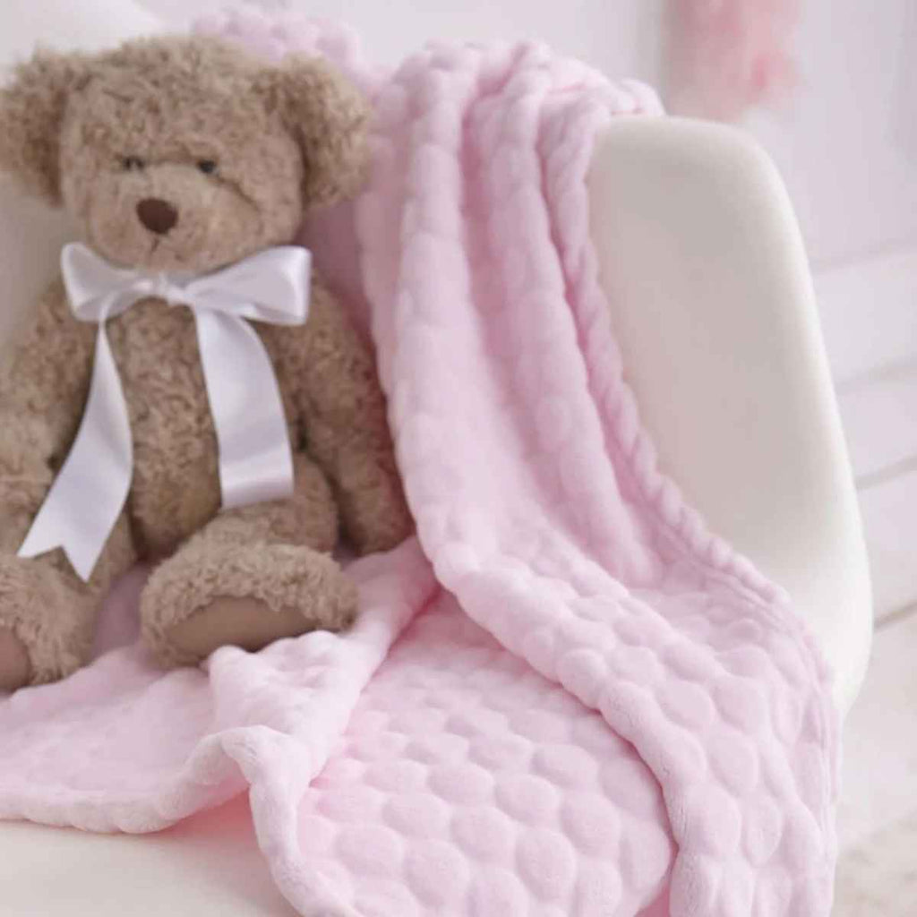 Brown teddy bear with a white bow sitting on a pink marshmallow blanket