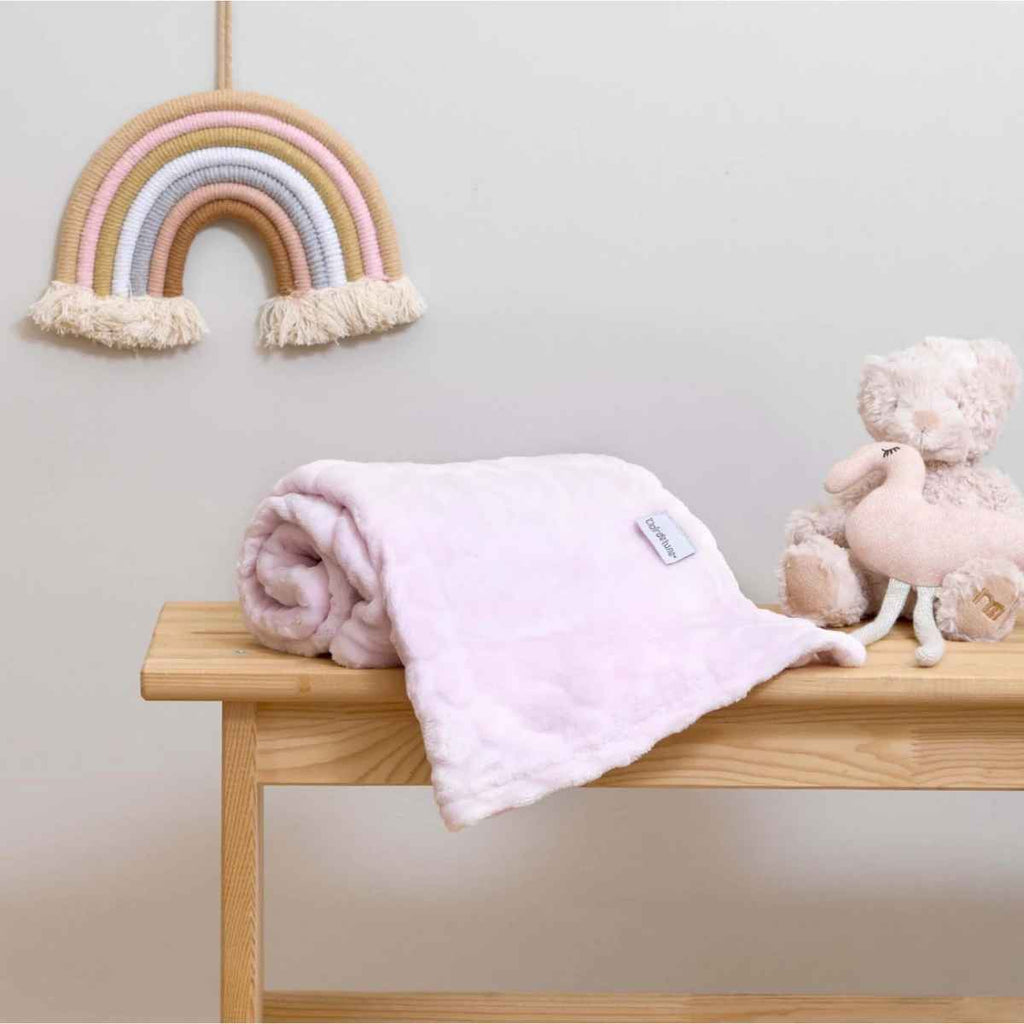 Pink marshmallow blanket on a wooden bench with a rainbow decoration and plush toy in the background.
