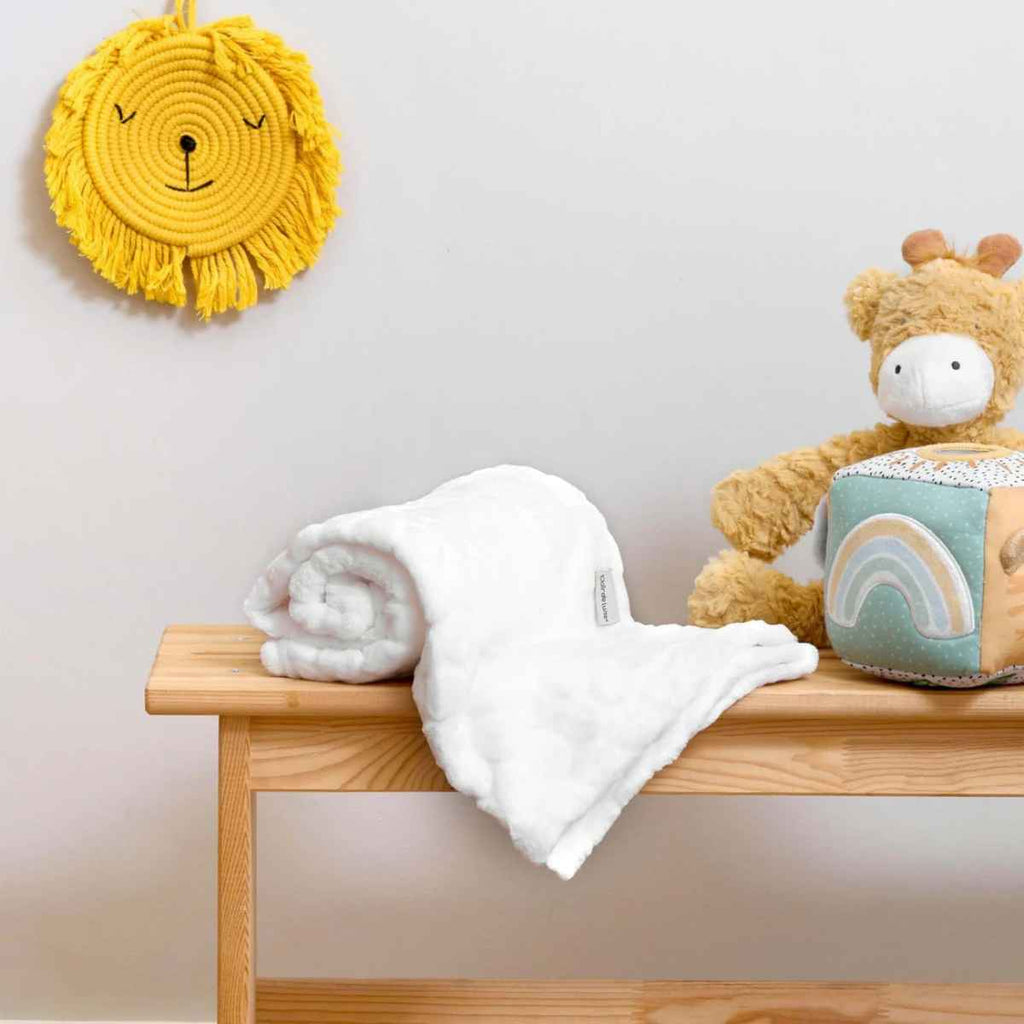 White blanket on a wooden table with a yellow lion wall decoration and teddy bear in the background.