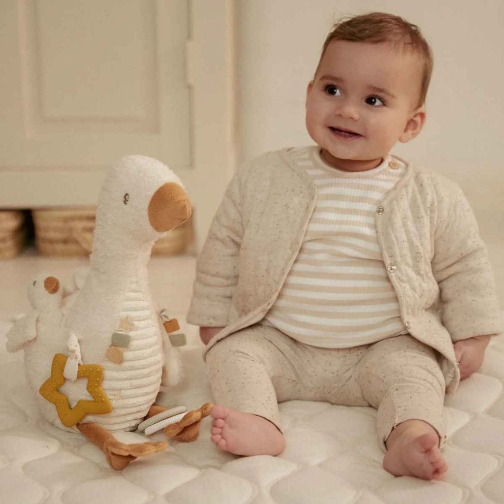 Baby sat beside an activity soft toy goose from Little Dutch.