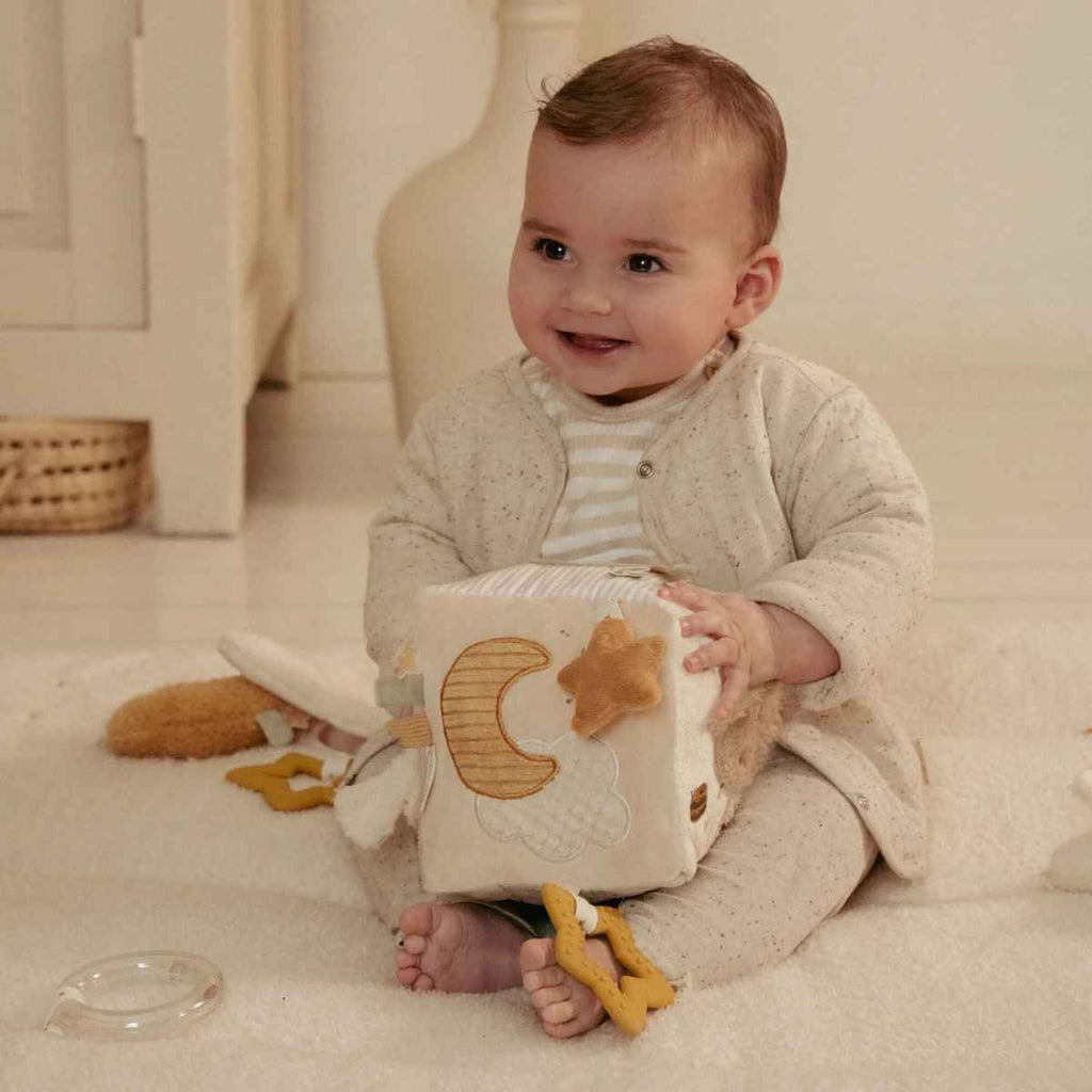Baby sitting on a light-colored floor holding a soft activity cube with star and moon designs.