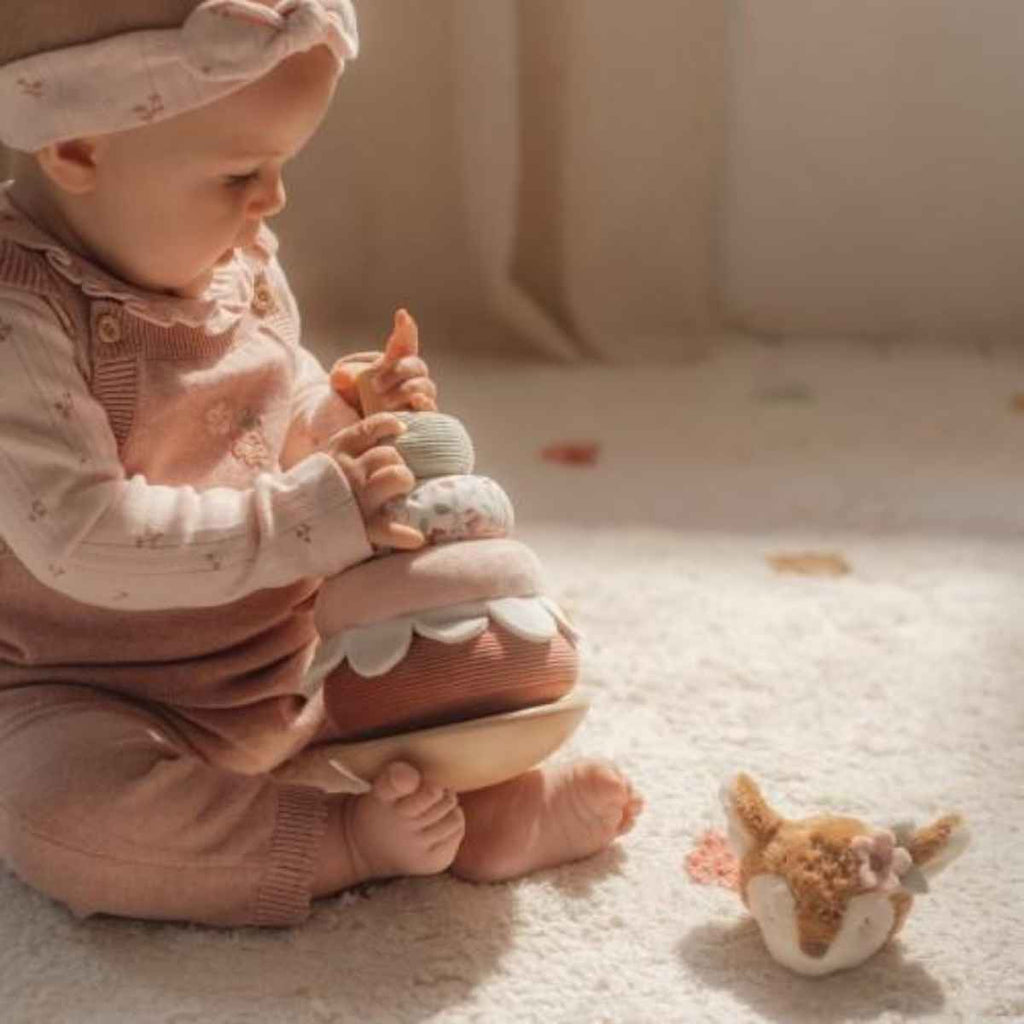 Baby in pink outfit holding Little Dutch Soft Rocking Ring Stacker in the fairy garden design.