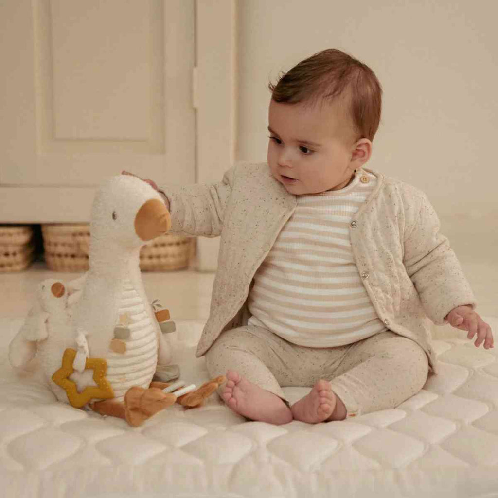 Baby playing with a plush goose activity toy in a softly lit room.