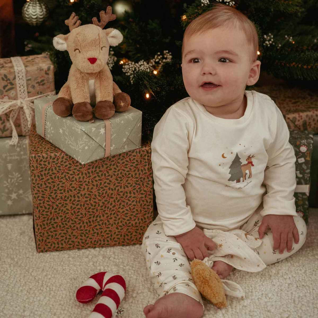 Baby sitting on the floor with a plush reindeer toy and Christmas presents in the background.