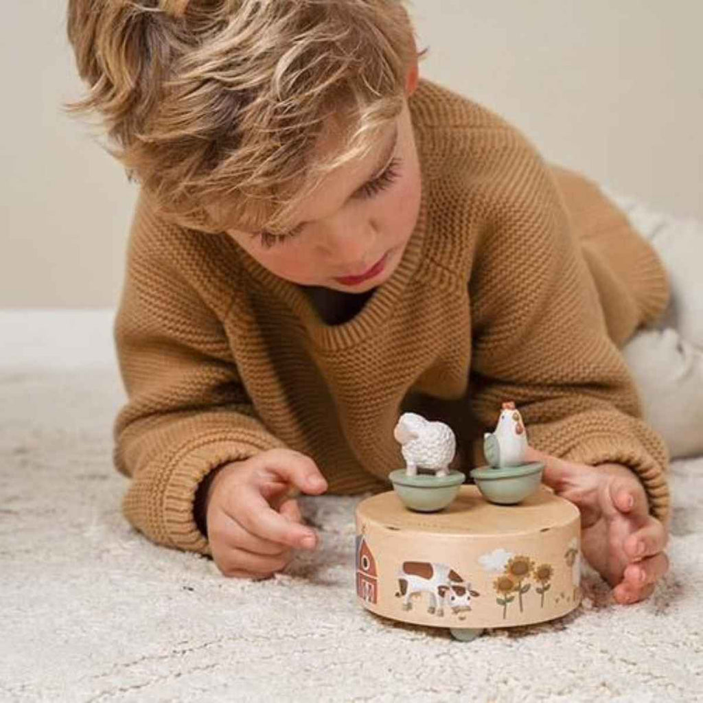 Child playing with a wooden musical farm toy featuring animal figures on a carpeted floor.