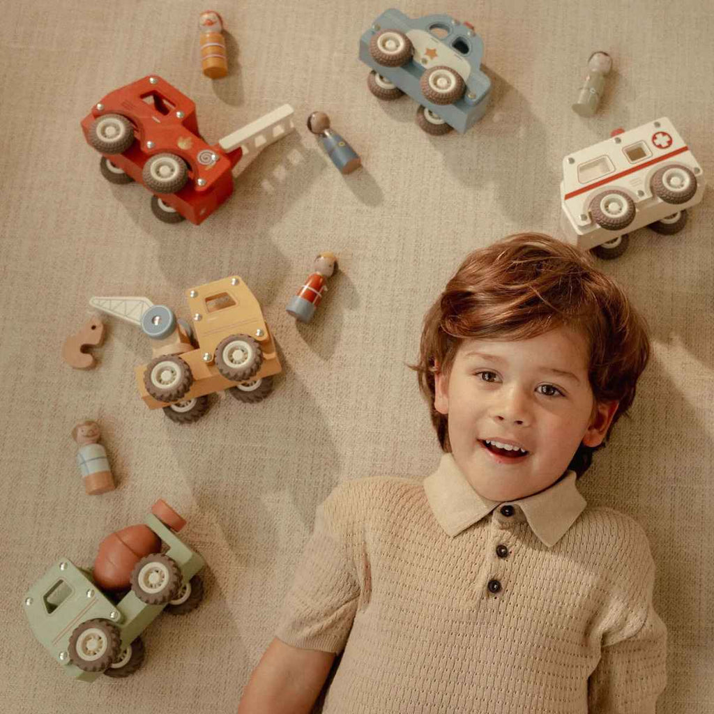 Child surrounded by wooden toy cars on a textured surface