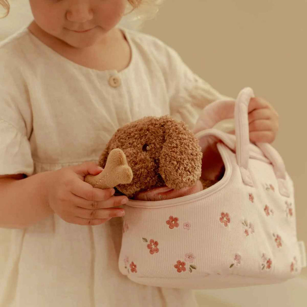 Child holding a teddy dog in a floral-patterned bag against a beige background