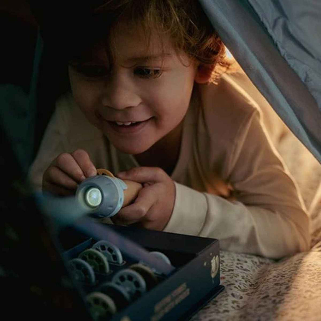 Child holding a flashlight projector under a blanket, likely in a bedroom setting