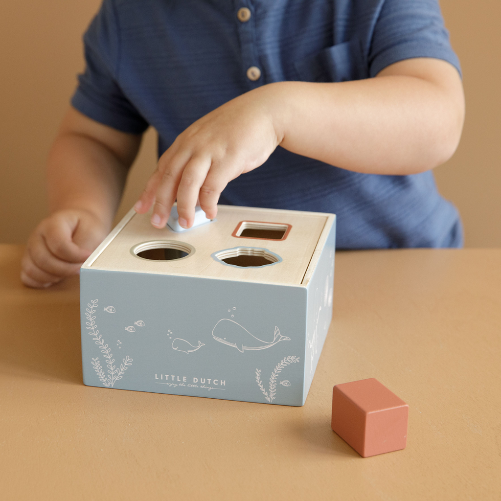 Child playing with a shape sorting toy from Little Dutch on a brown background