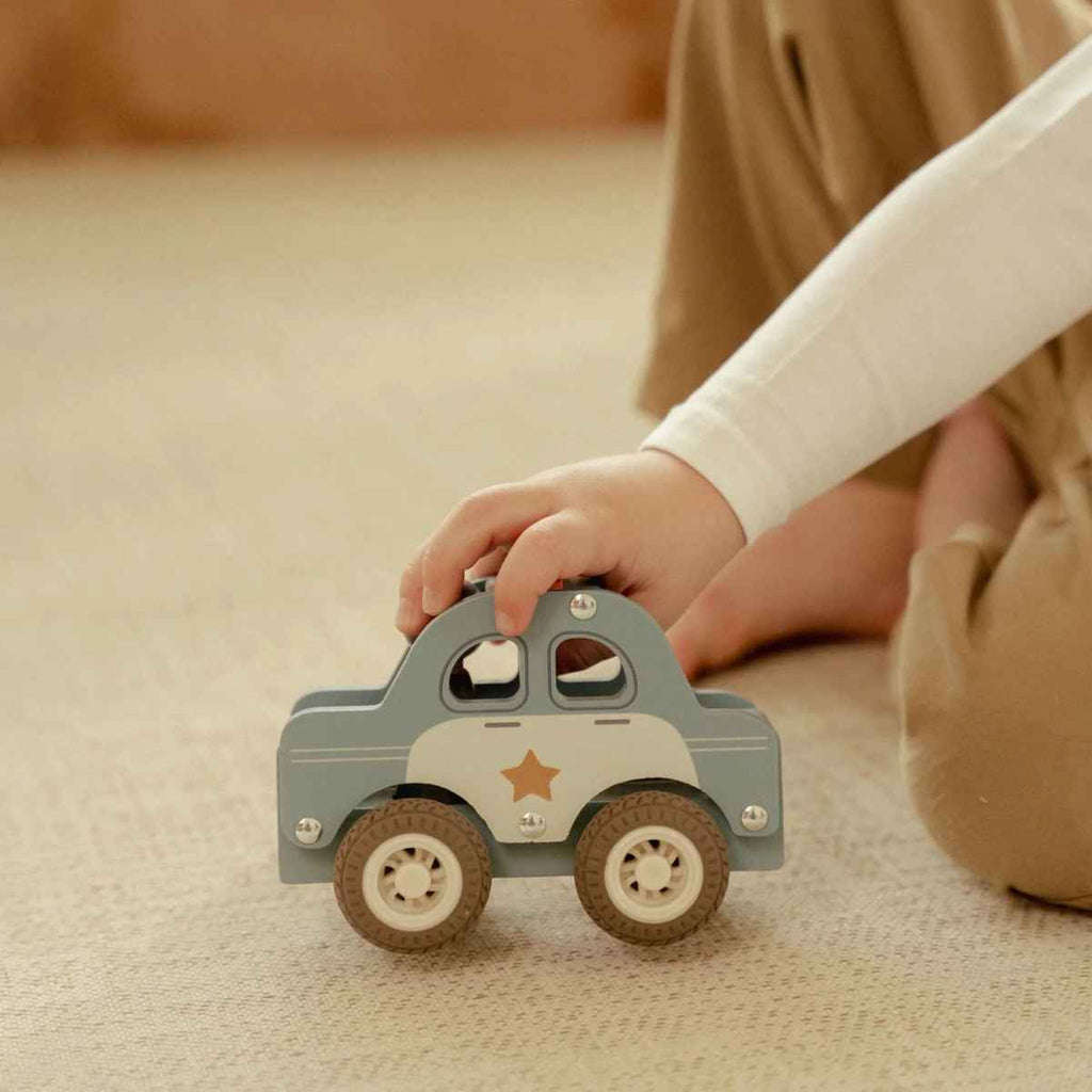Child's hand holding a wooden toy car on a soft surface