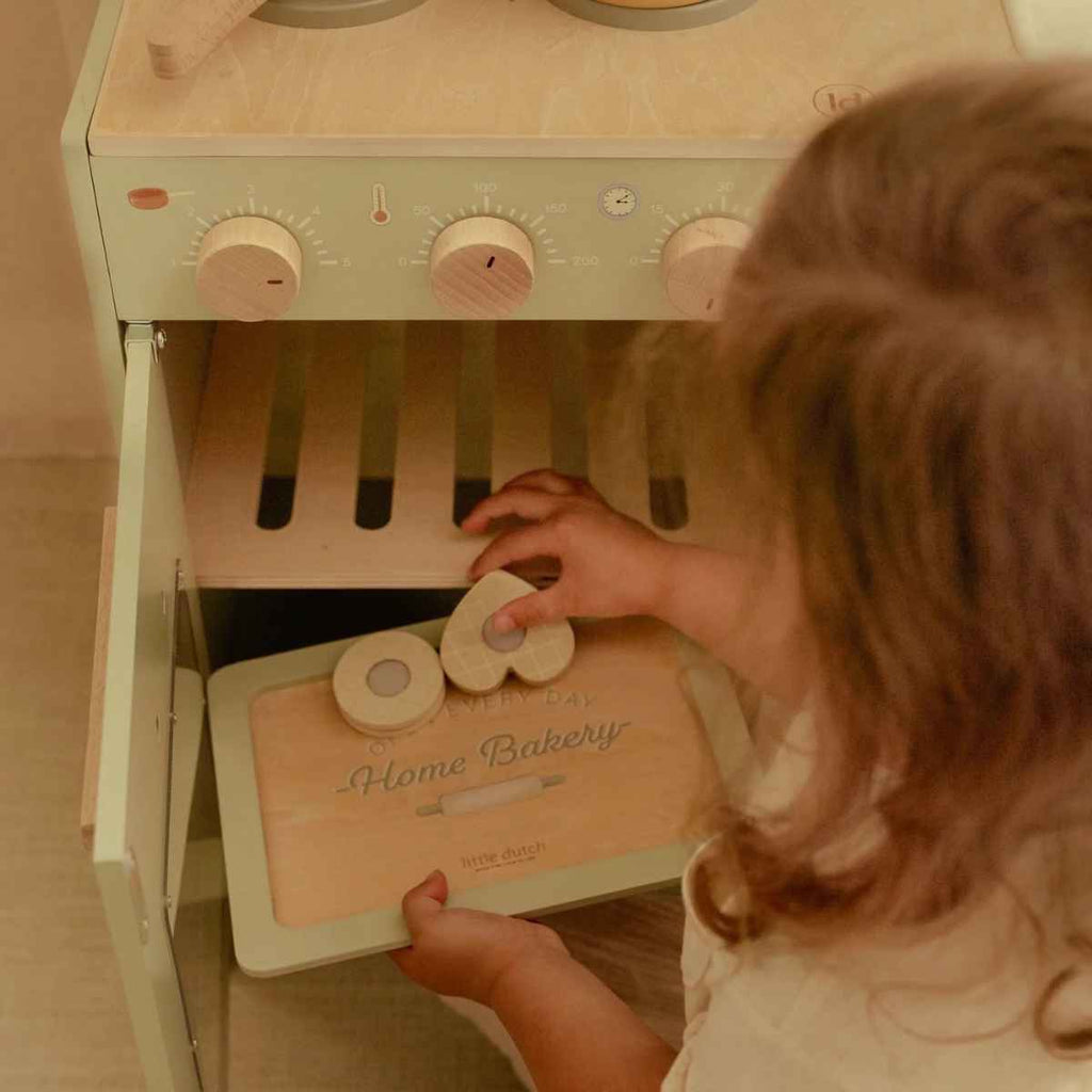 Child putting wooden toy biscuits into wooden kitchen oven.