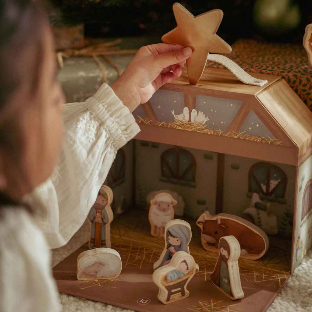 Child holding a star above a wooden nativity scene set.