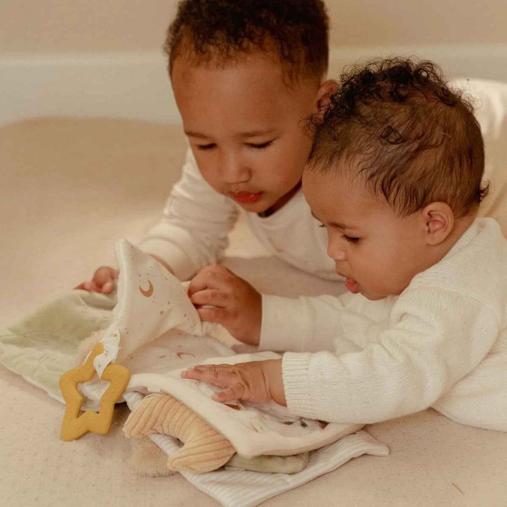 Two children playing with soft activity book together on a soft floor.