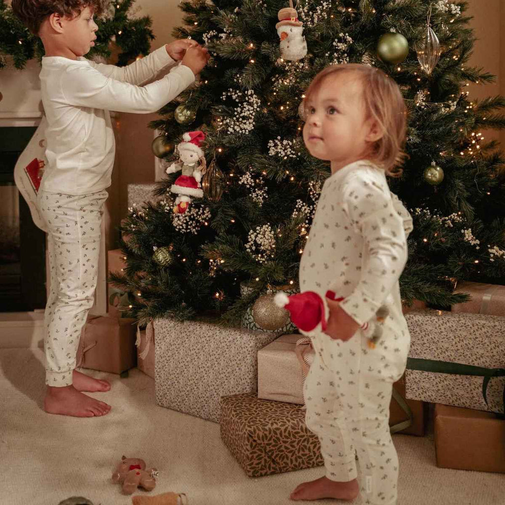 Two children in pajamas decorating a Christmas tree with presents underneath.