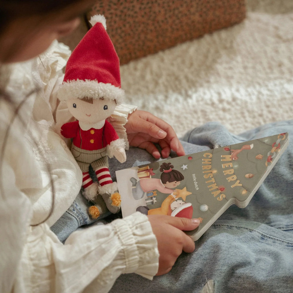 A child  holding a small elf doll and a Christmas book.