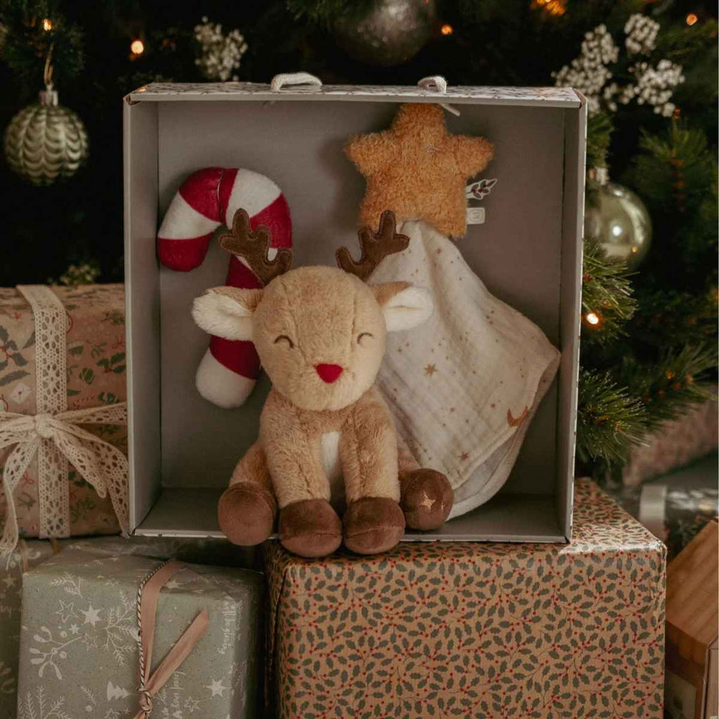 Plush reindeer toy with candy cane and star in a giftbox, Christmas tree and presents are in the background
