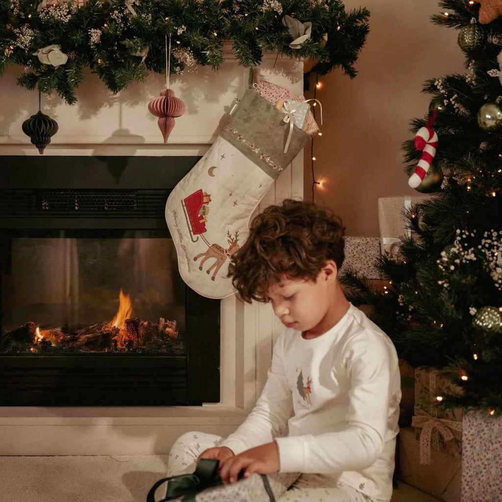 Child opening a gift in front of a fireplace with Christmas stockings and tree.