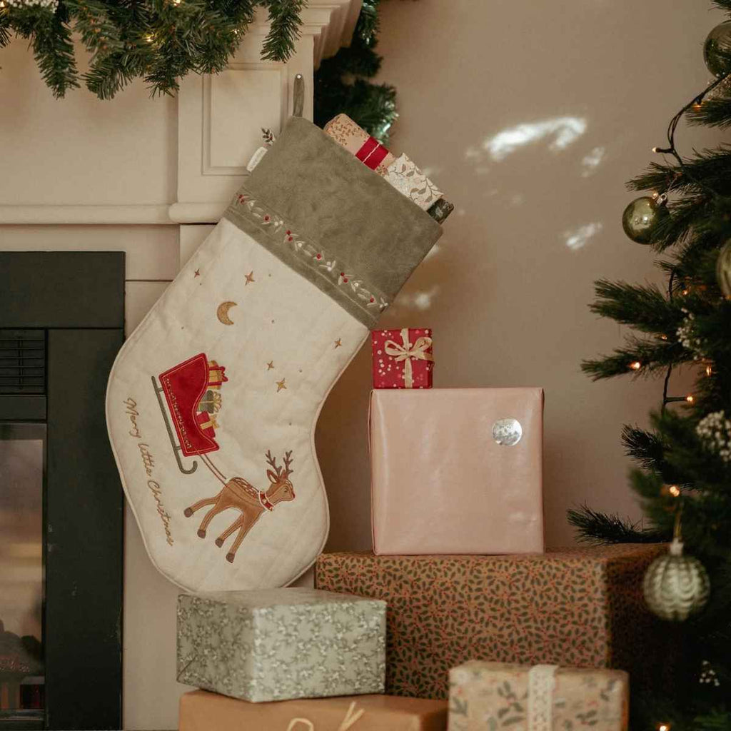 Decorative Christmas stocking with festive design on a pile of gifts next to a tree.