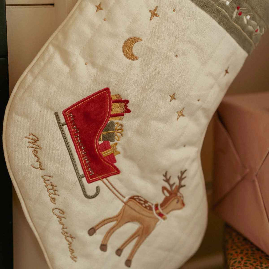 Christmas-themed stocking with a reindeer and sleigh design on a beige background.
