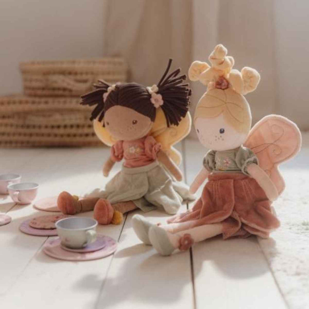 Two plush fairies, one with dark hair and the other with blonde hair, sitting on a wooden floor having a tea party.