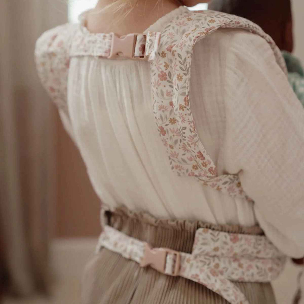Girl wearing a floral-patterned baby carrier buckled in at the back