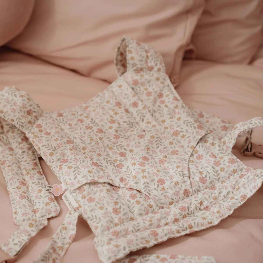 Floral-patterned baby doll carrier on a pink blanket