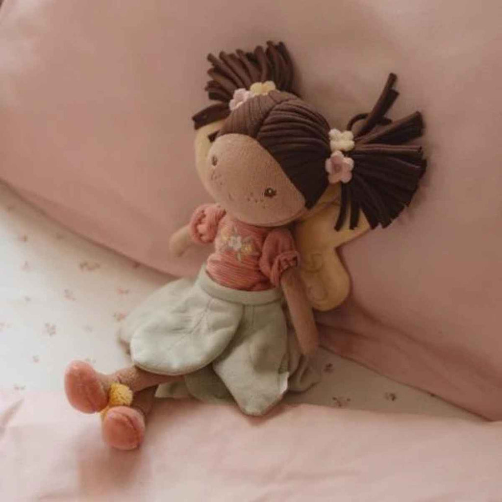 Plush fairy toy with brown hair in a pink shirt and green leafy skirt on a pink pillow