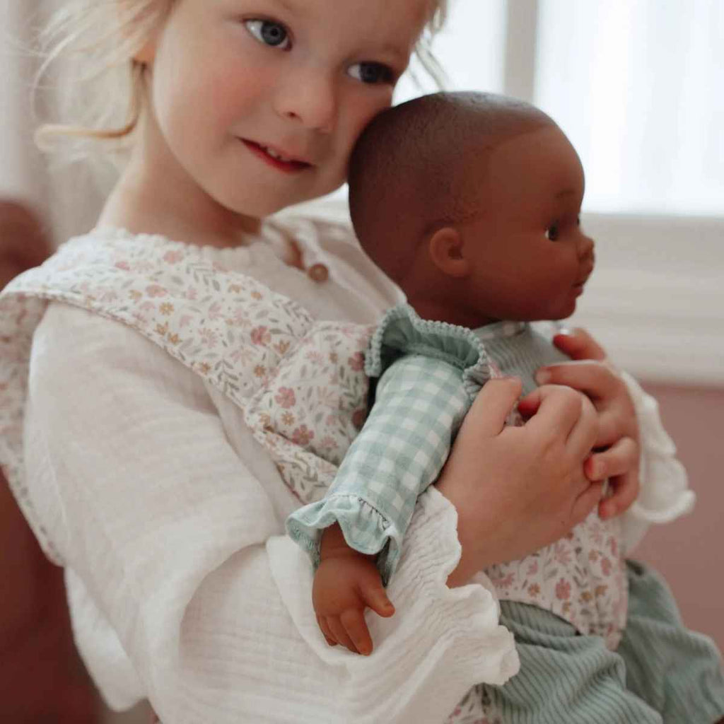 Child holding a babydoll in a carrier with a neutral background