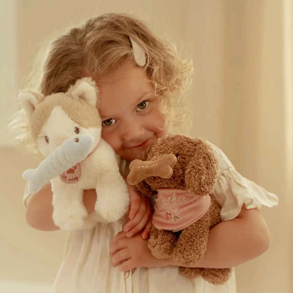 Child holding two stuffed animals against a plain background