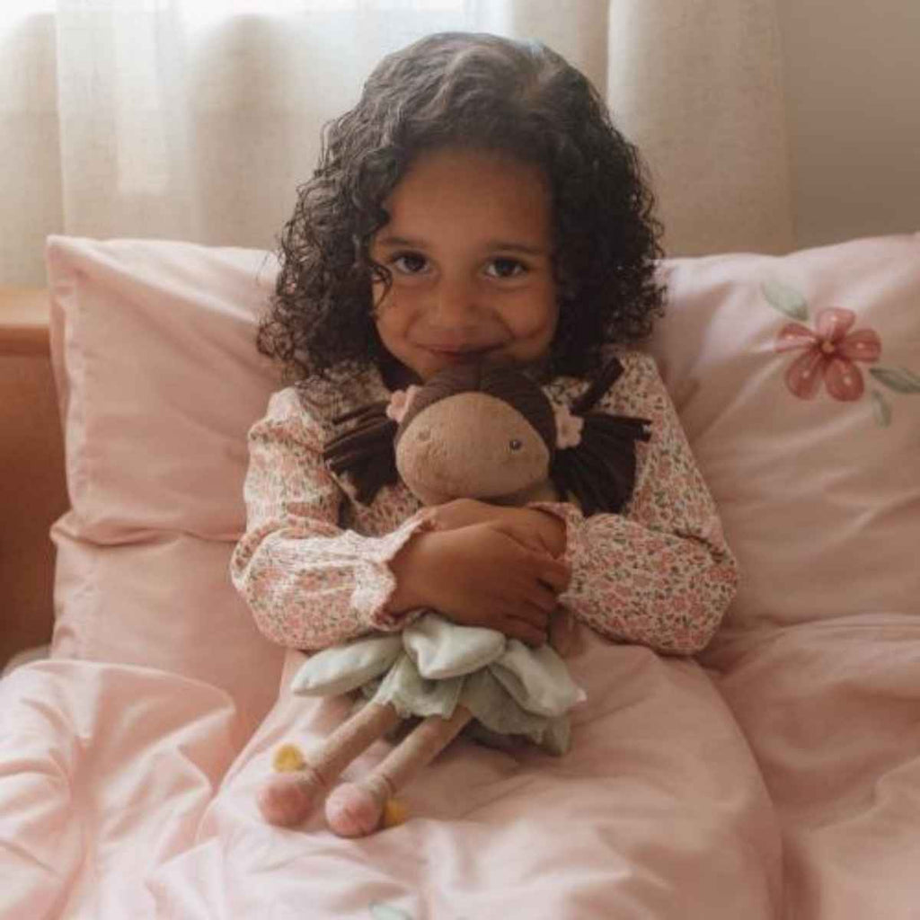 Young girl holding Fairy Evi in a bed with pink bedding