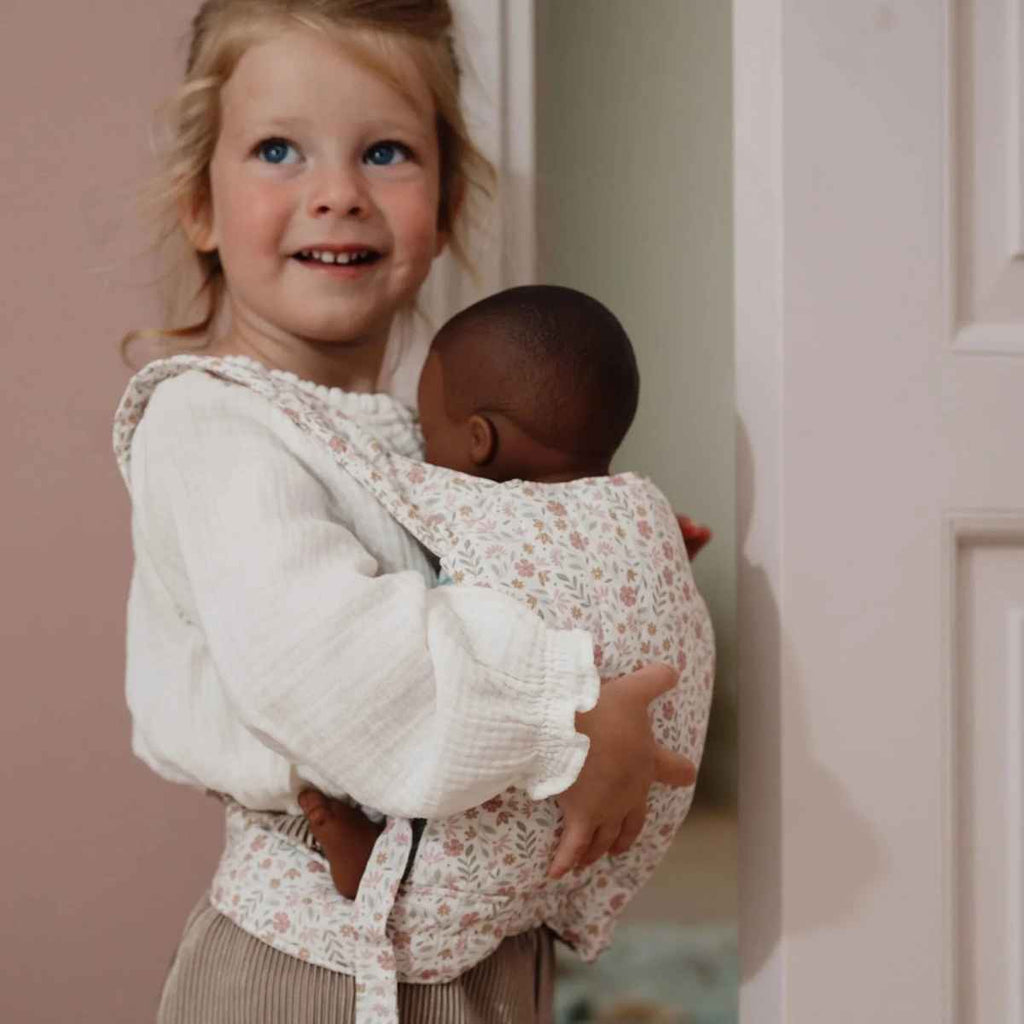 Girl holding her baby doll in a floral patterned baby carrier.
