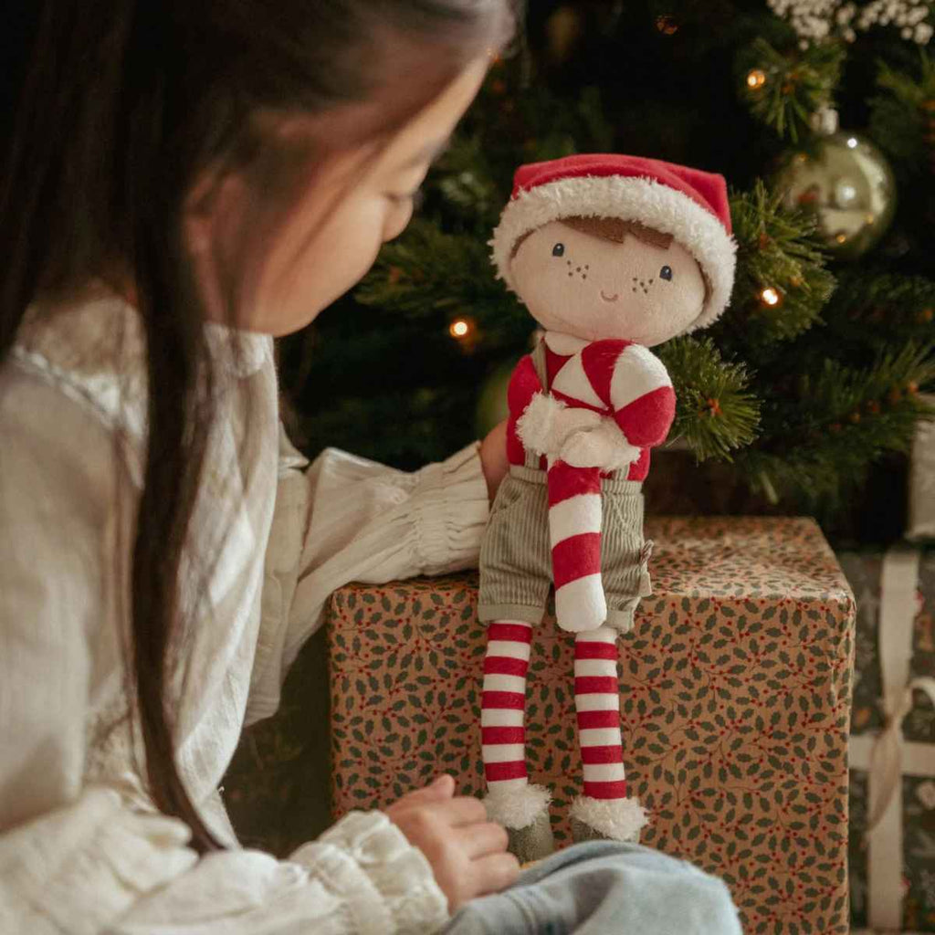Child with a Christmas-themed doll in front of a decorated tree