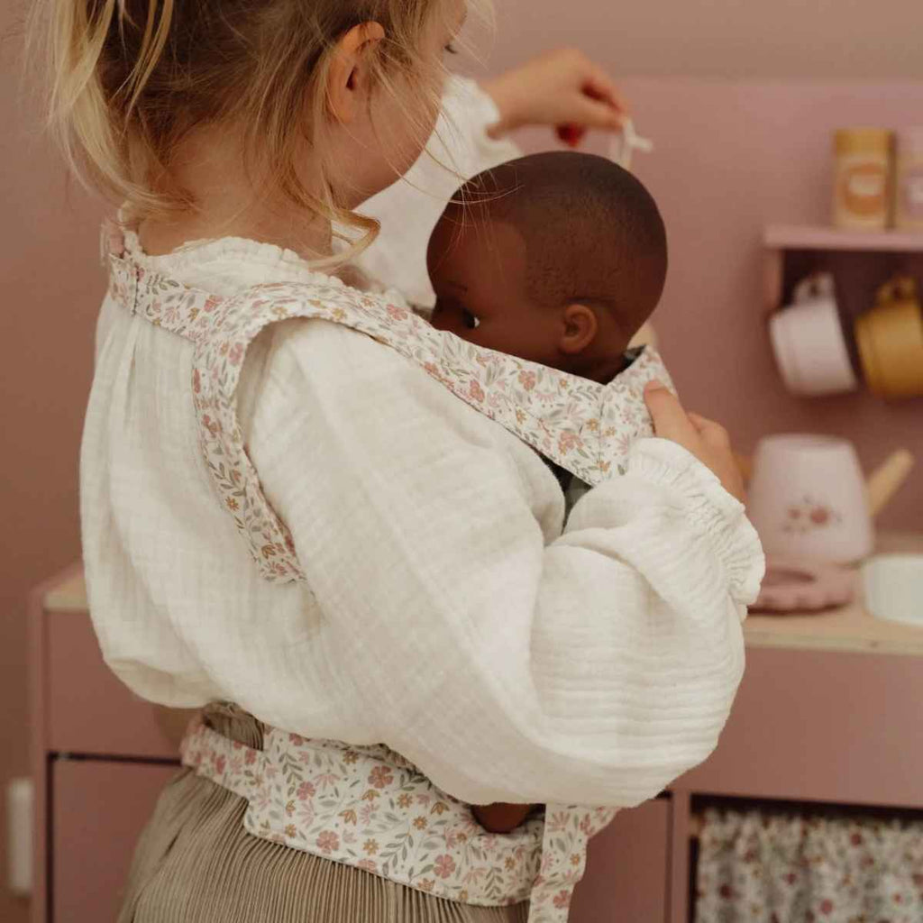 Girl playing with baby carrier in a kitchen setting.