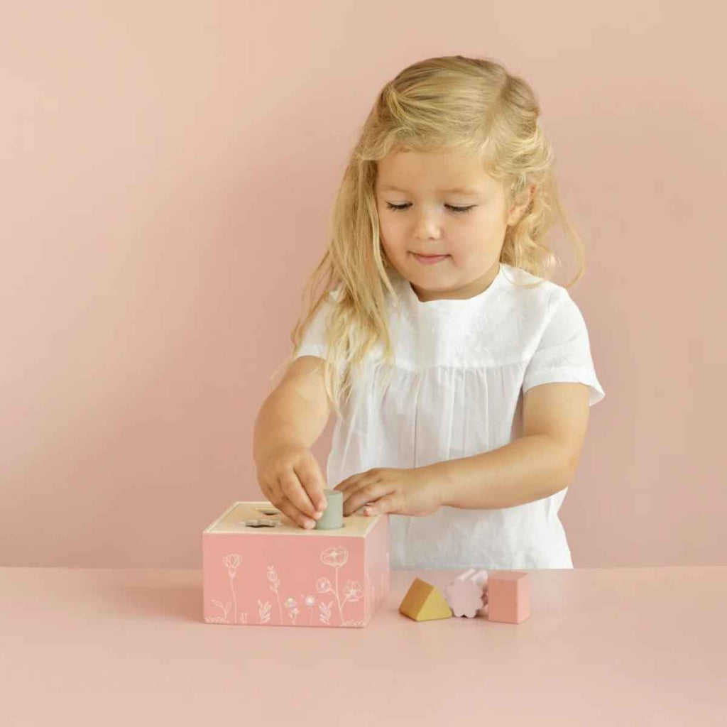 Young girl playing with a pink wooden shape sorter against a pink background
