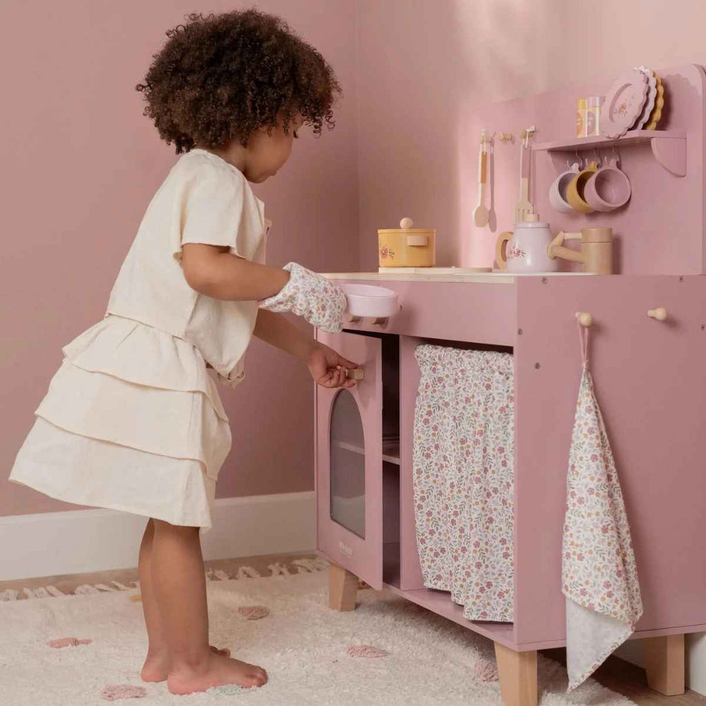Child playing with a pink toy kitchen set against a pink wall.