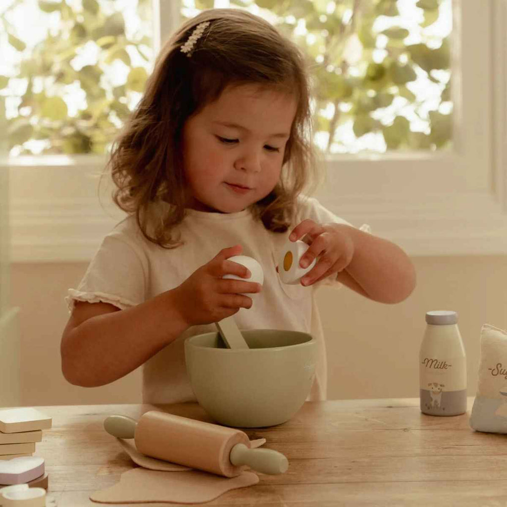 Child playing with wooden kitchen and baking toys at a table