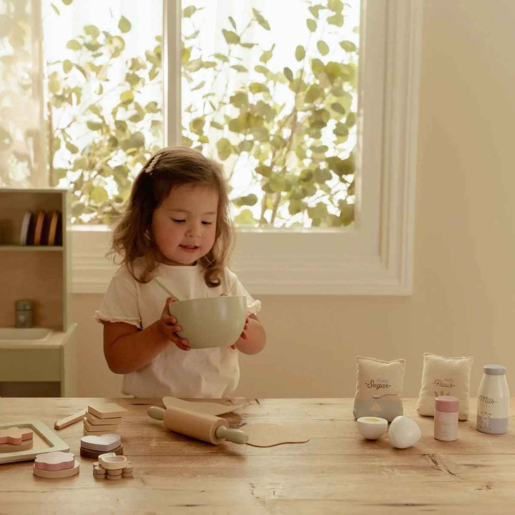 Child playing with baking toys at a table near a window
