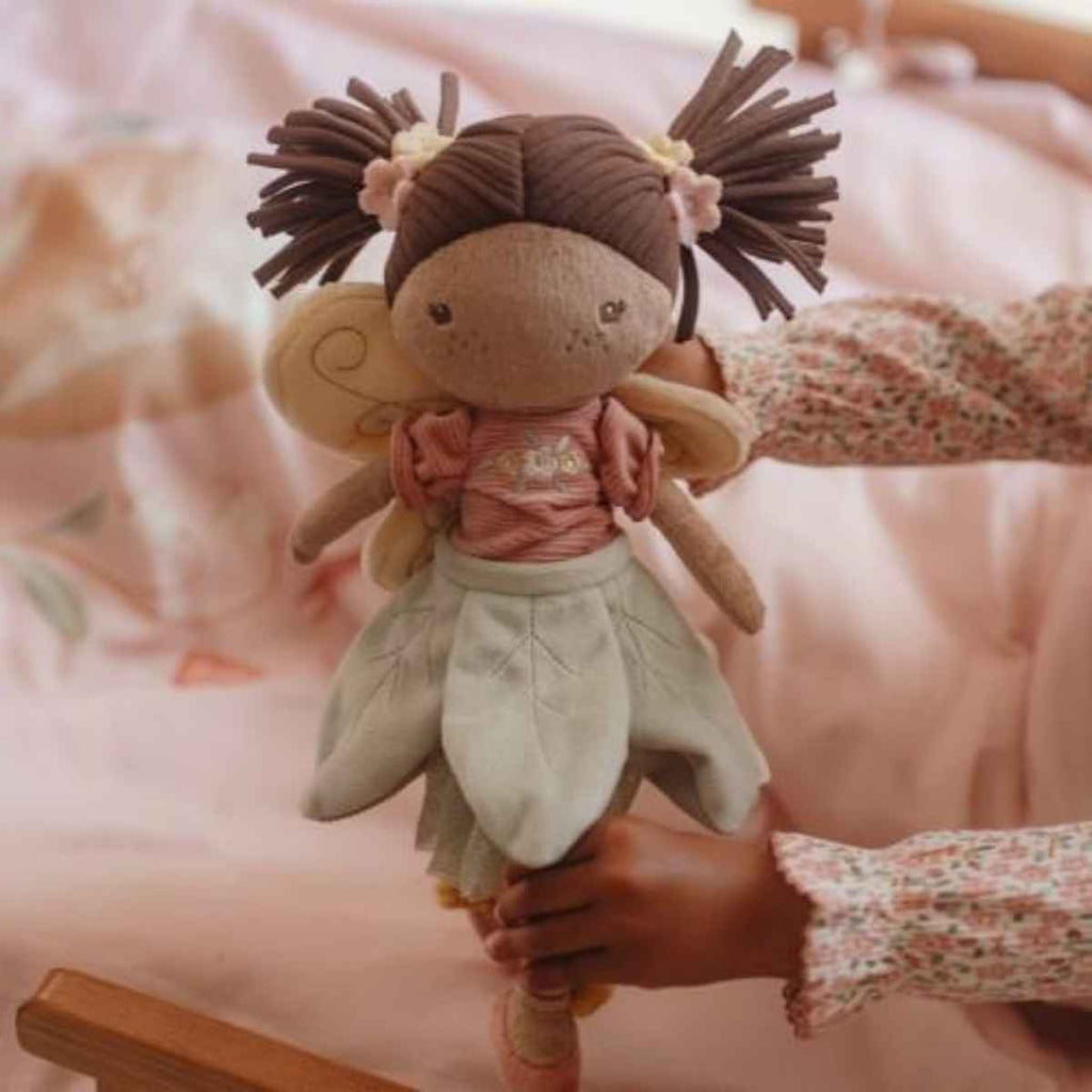 Hand holding a soft toy with braided hair and floral dress on a blurred background