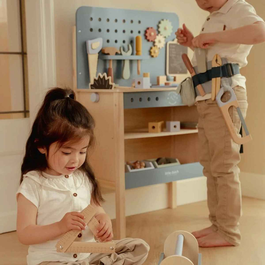 Two children playing with a toy workbench set in a room.