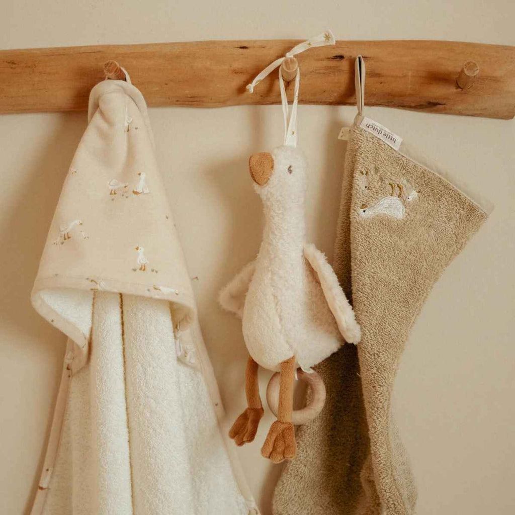 Baby towels and a goose music box hanging on a wooden rack against a beige wall.