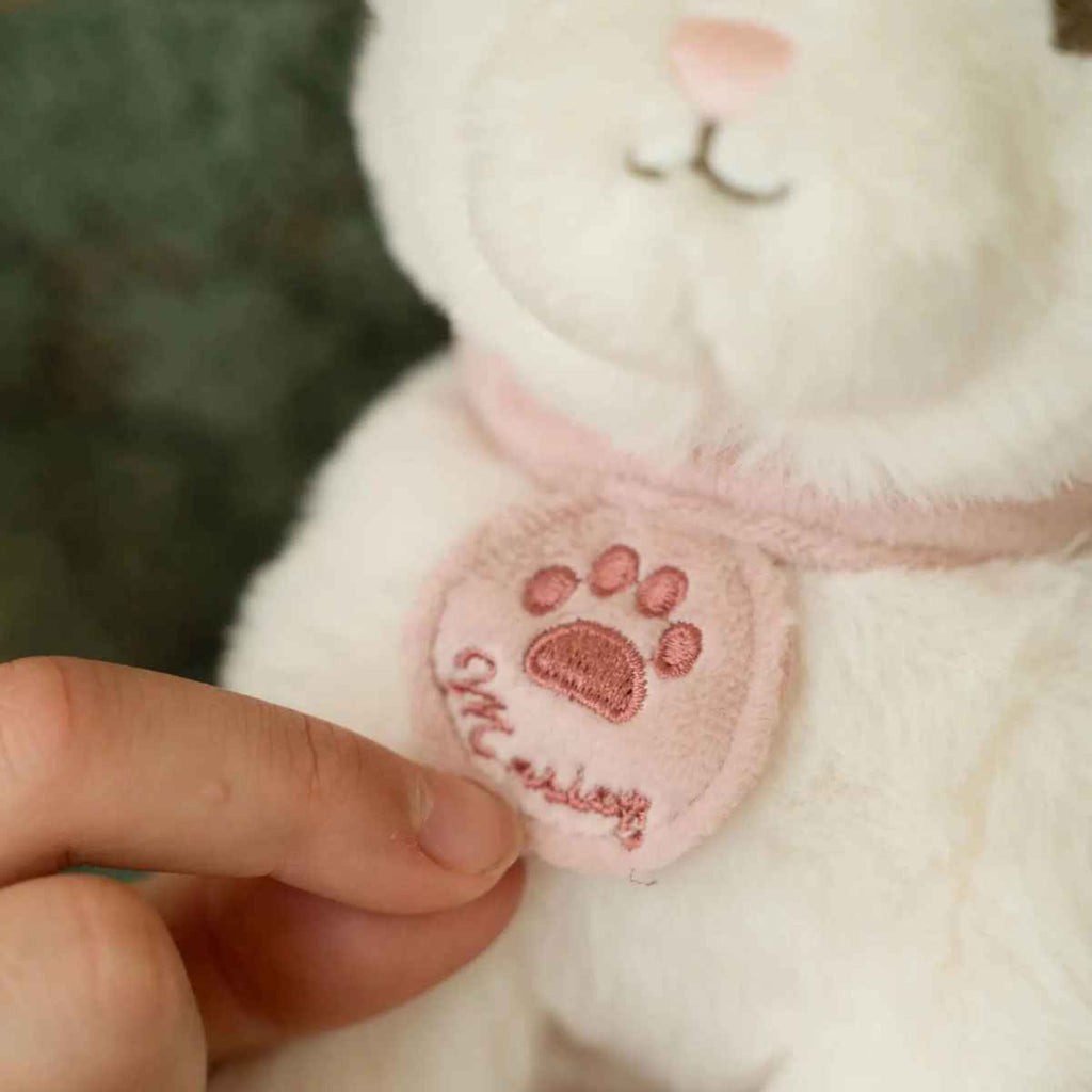 Close-up of a cat plush with a pink paw print collar held by a hand.