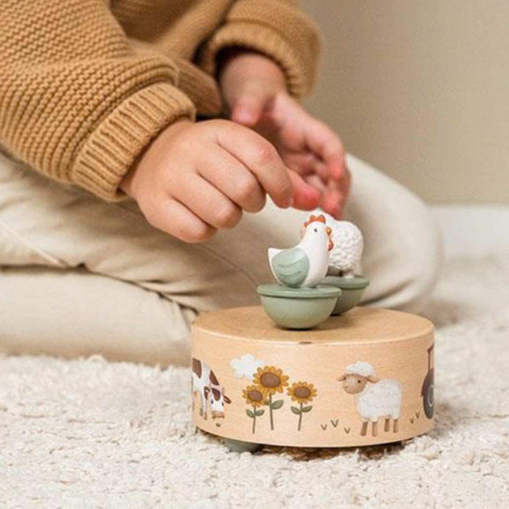 Child playing with a wooden toy box featuring animal illustrations and wooden farm animals