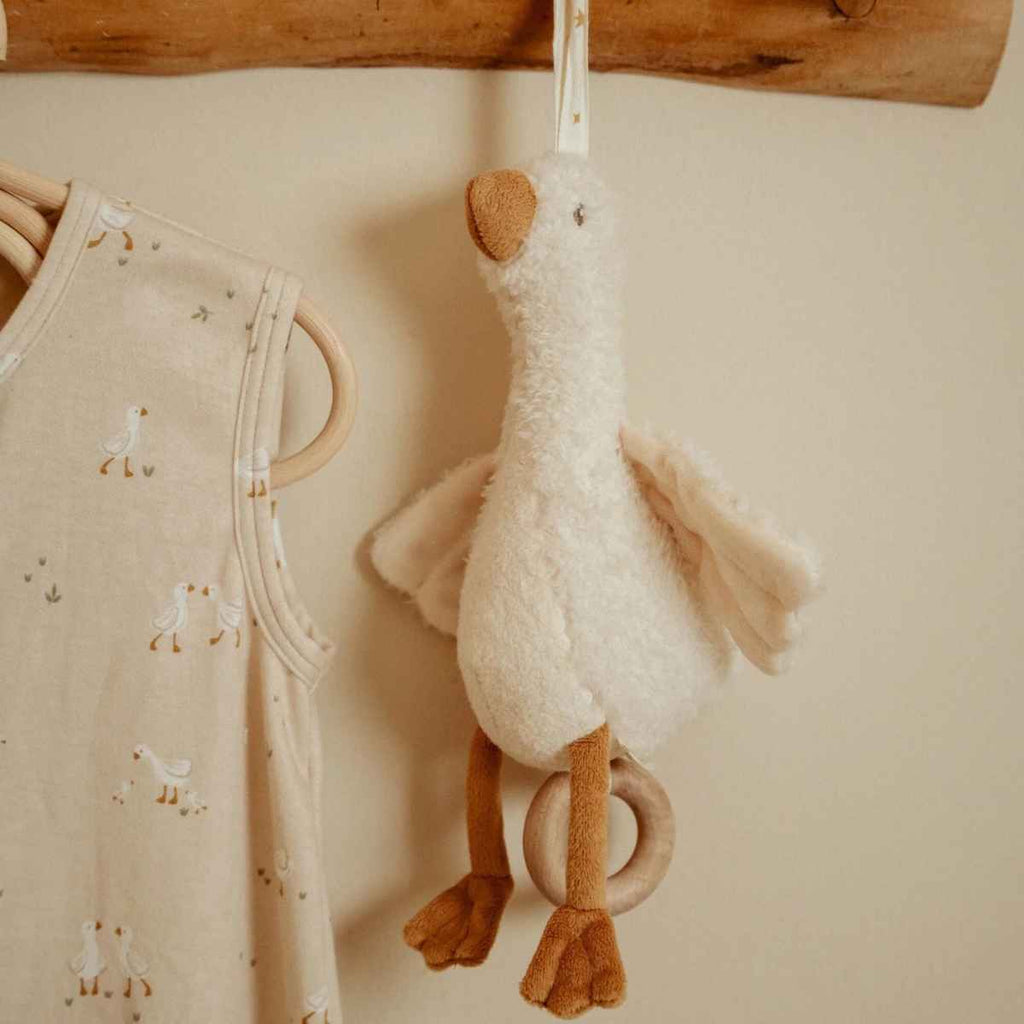 Plush music box goose hanging on a wooden hook next to baby clothing on a beige background
