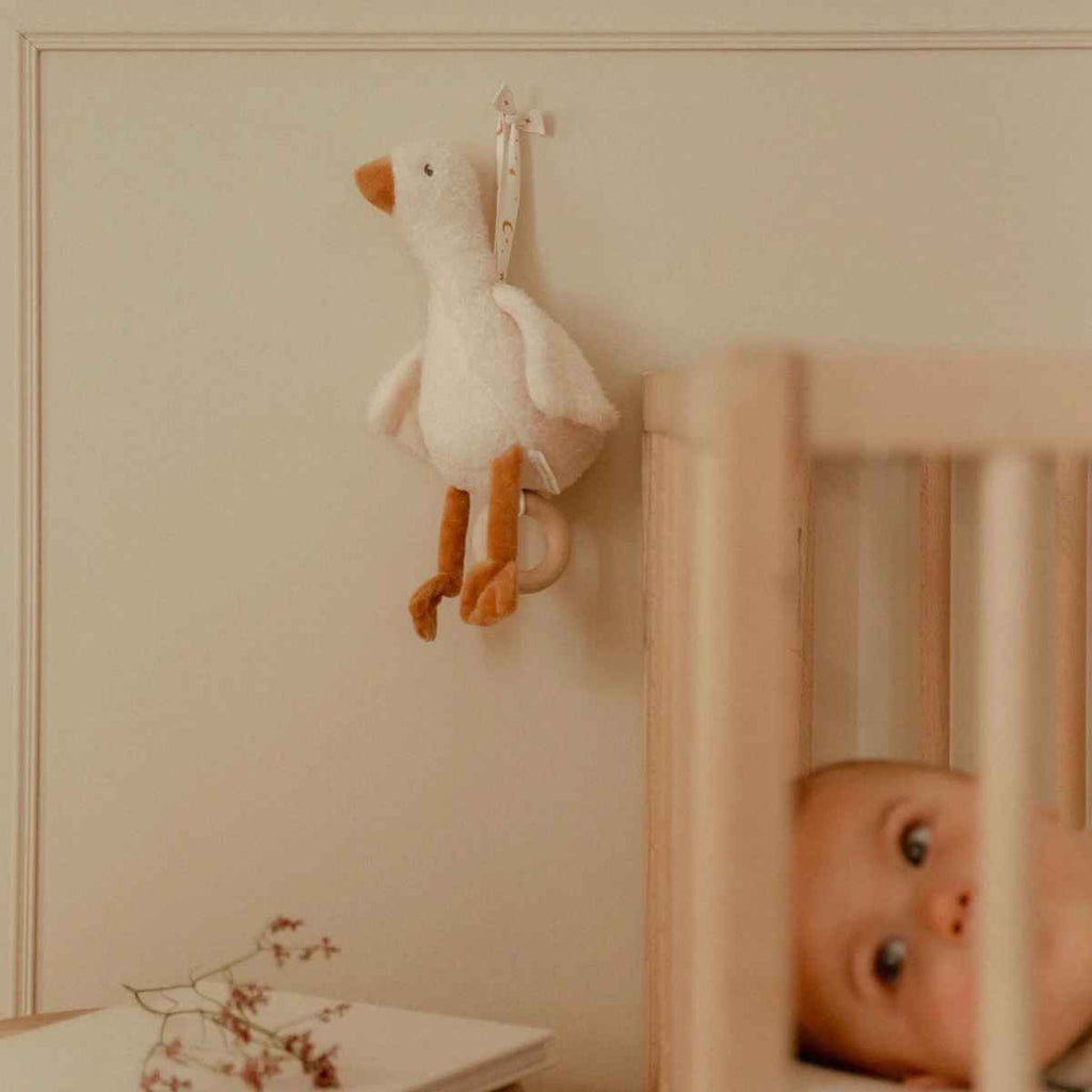 Baby in a crib with a goose music box hanging above, in a softly lit room.