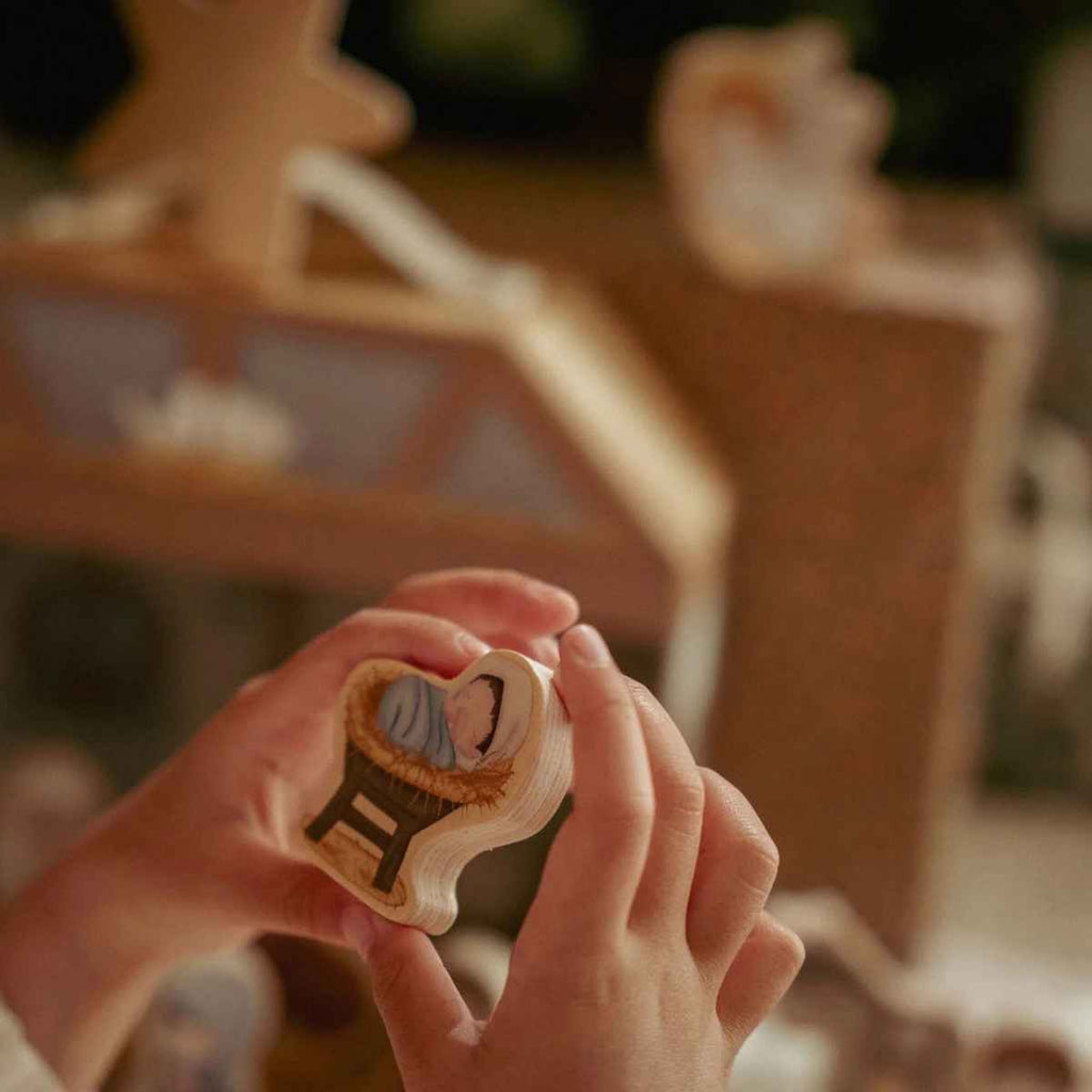 Wooden nativity baby Jesus held by hands with blurred background