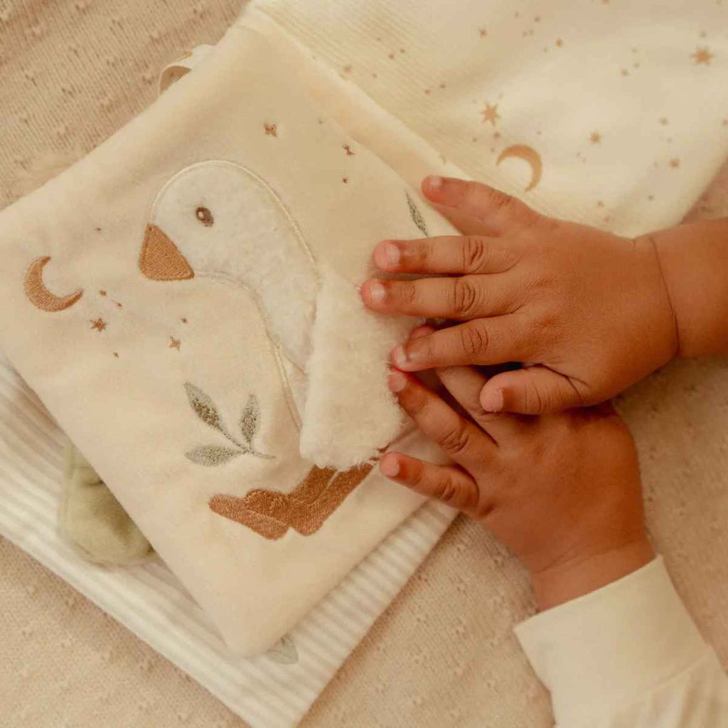 Soft activity book open on a page with a soft goose and hands playing with it.