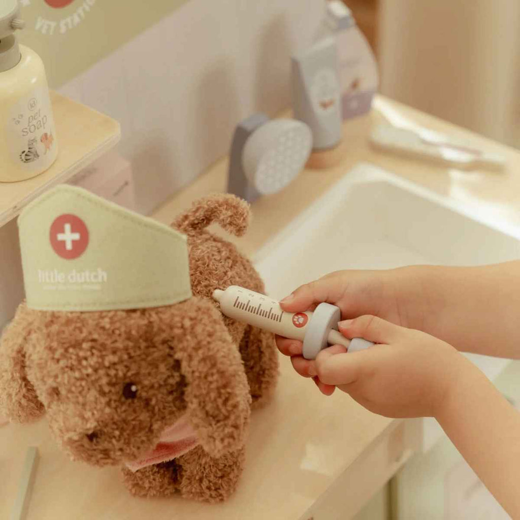 Teddy dog with a vet hat being given an injection by a hand in a vet setting.