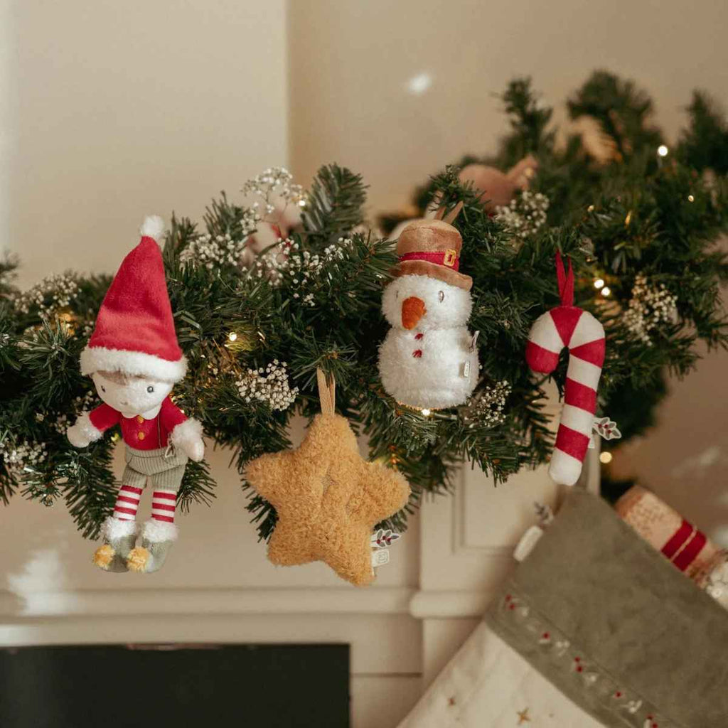 Decorative Christmas garland with plush Jim, snowman, star and candy cane decorations on a fireplace.